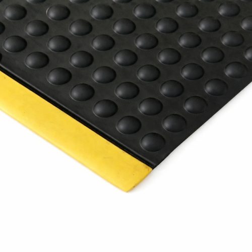 Close-up of a black anti-fatigue rubber mat with raised bubble surface and yellow beveled safety edge on a white background.